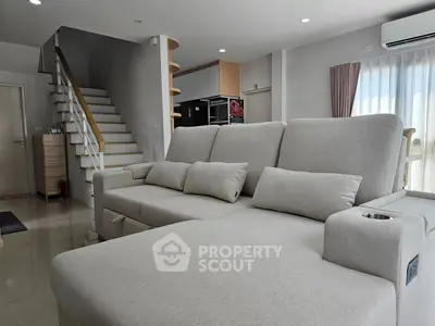 Modern living room with cozy sectional sofa and elegant staircase in bright, airy space.