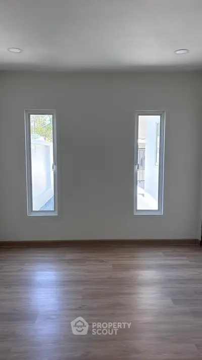 Bright empty room with two tall windows and wooden flooring, perfect for customization.