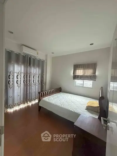 Cozy bedroom with wooden flooring and elegant curtains, featuring a classic wooden bed and ample natural light.