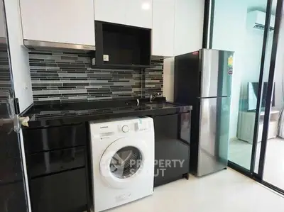 Modern kitchen with sleek black countertops, washing machine, and stainless steel fridge.