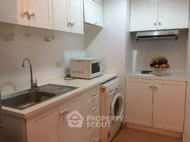 Compact kitchen with white cabinets, washing machine, and microwave, ideal for efficient urban living.