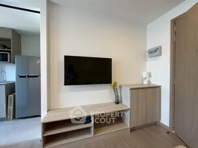 Modern living room with wall-mounted TV and sleek wooden furniture, adjacent to a compact kitchen area.