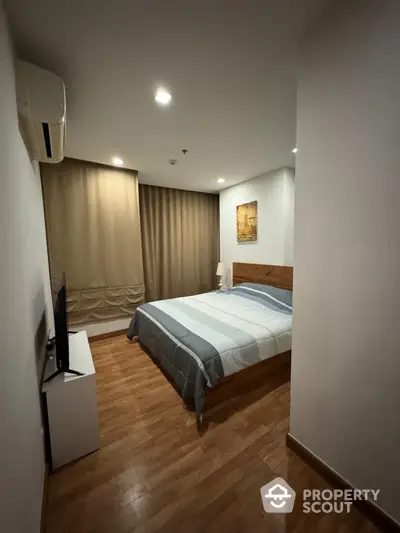 Cozy bedroom with polished wooden flooring, a comfortable queen-sized bed, and modern amenities, perfect for restful nights in a serene urban home.