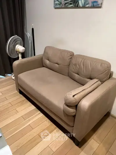 Cozy living room with a comfortable beige sofa and wooden flooring, perfect for relaxation.