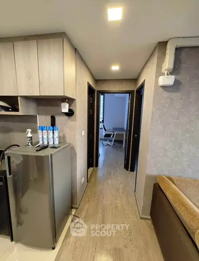 Modern apartment interior with compact kitchen and hallway leading to a study room, featuring sleek design and wood flooring.