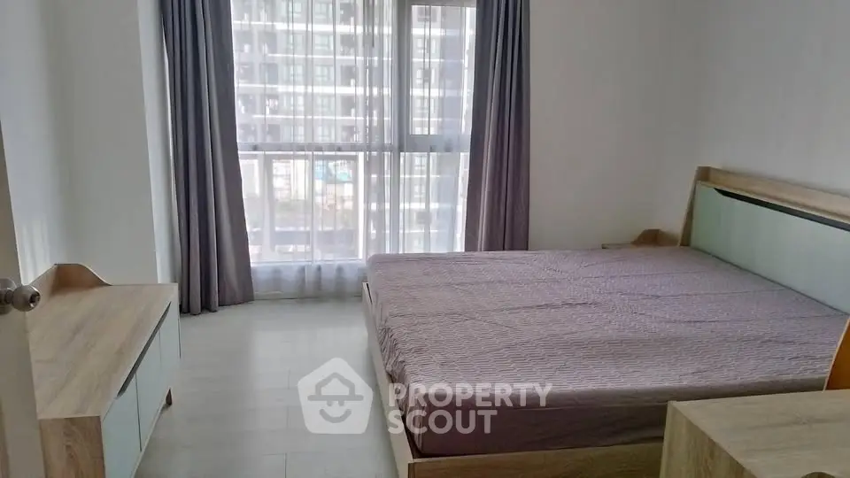 Spacious bedroom with large window and modern furnishings in a high-rise apartment.