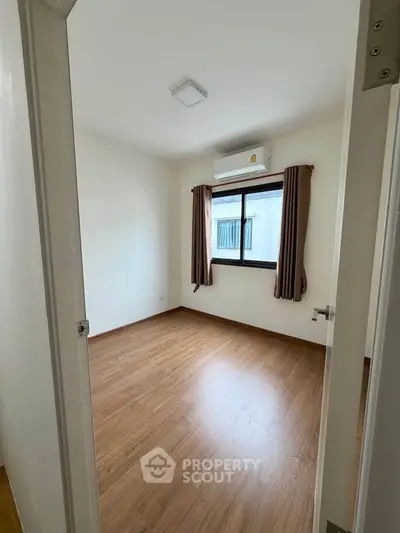 Spacious bedroom with wooden flooring and large window in modern apartment.