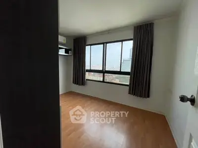 Spacious bedroom with large window offering city views and wooden flooring.