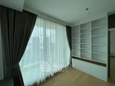 Spacious room with large window and built-in shelves, offering city views.
