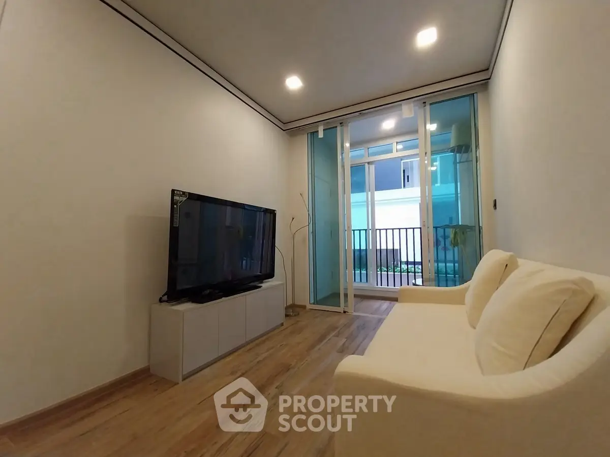Modern living room with sleek design and large TV, featuring a cozy sofa and glass doors leading to a balcony.