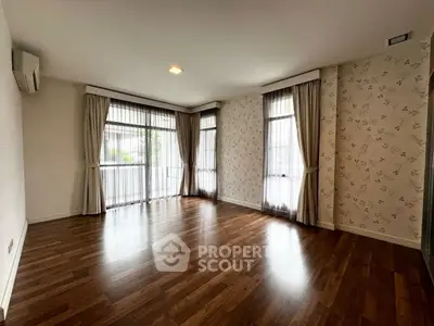 Spacious empty living room with elegant wooden flooring and large windows for natural light.