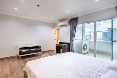 Spacious bedroom with balcony access and modern furnishings in a high-rise apartment.