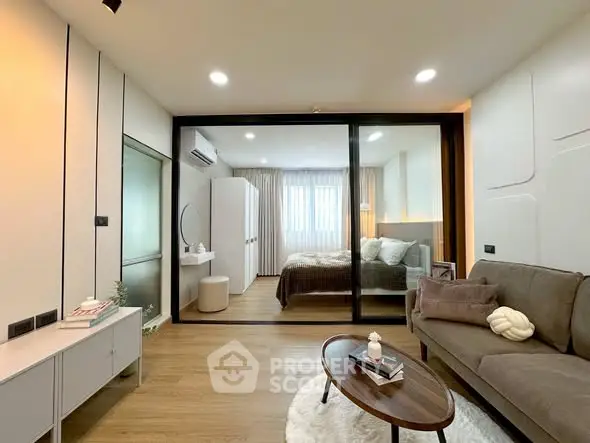 Modern living room with cozy bedroom view through glass partition, stylish decor and wooden flooring.