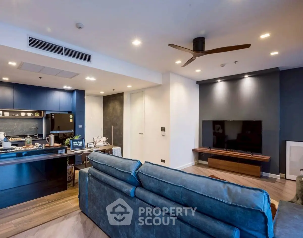 Modern living room with open kitchen, blue sofa, and wall-mounted TV in stylish apartment.