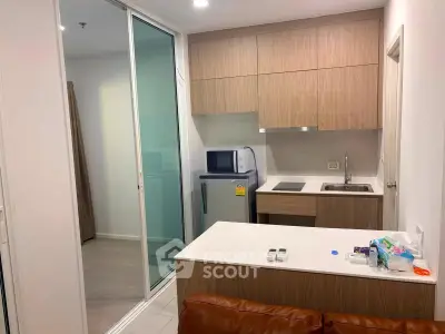 Modern compact kitchen with wooden cabinets and sleek appliances in a cozy apartment setting.