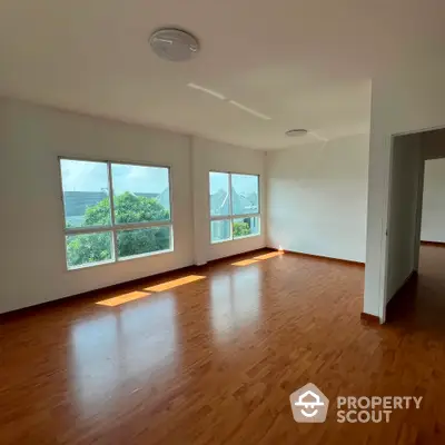 Spacious sunlit living room with large windows and wooden flooring