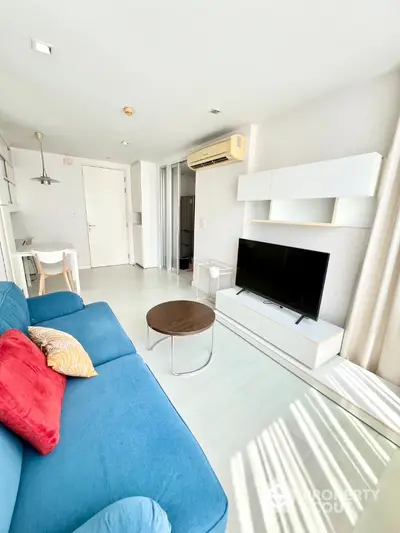 Bright and airy modern living room with a vibrant blue sofa, sleek white entertainment unit, and ample natural light streaming in, perfect for relaxed living and entertaining.