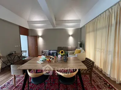 Spacious living room with modern decor and natural light, featuring a stylish dining area and cozy seating.