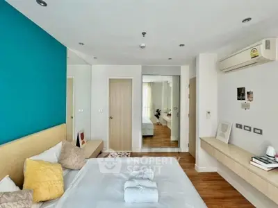 Modern bedroom with teal accent wall, mirrored closet, and wooden flooring.