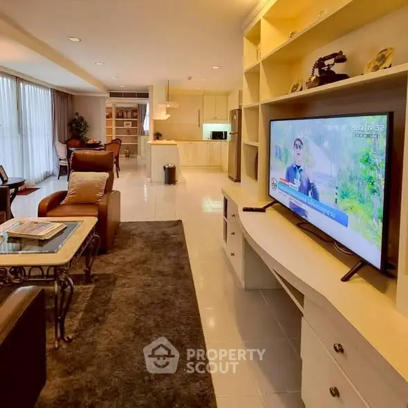 Spacious living room with modern decor and large TV, open layout to kitchen area.