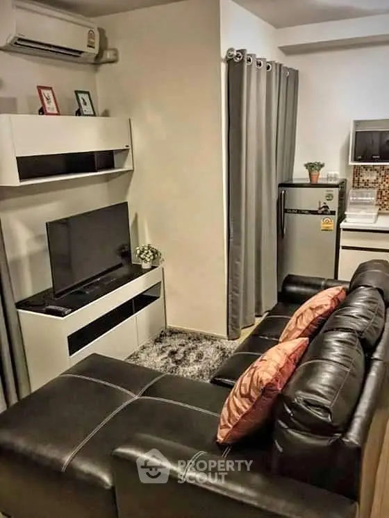 Cozy modern living room with leather sofa, TV, and compact kitchen area.