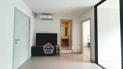 Modern apartment interior with TV, air conditioning, and open doorway to bedroom and bathroom.