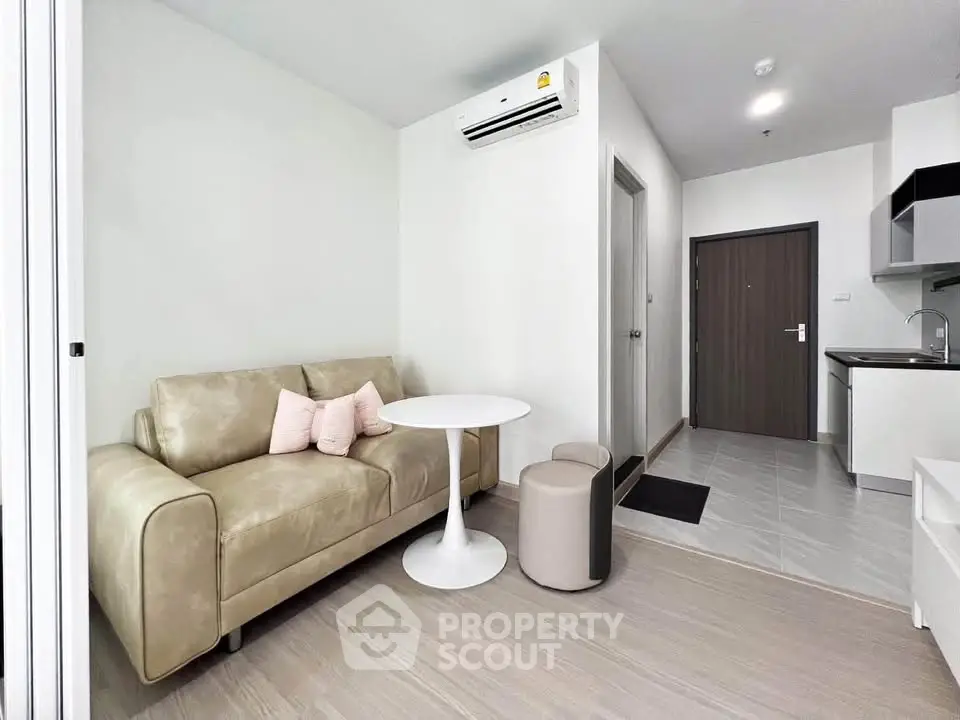 Modern living room with beige sofa, round table, and sleek kitchen in a stylish apartment.