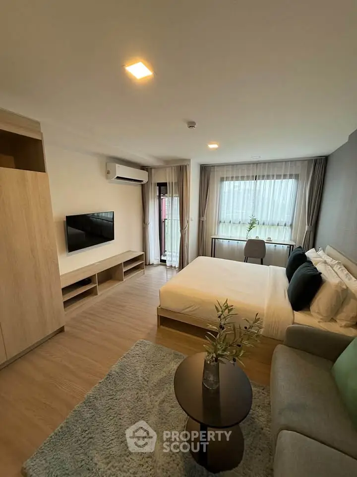 Modern bedroom with stylish decor and natural light, featuring a cozy bed and sleek TV setup.