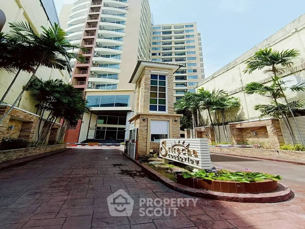 Modern high-rise building entrance with landscaped driveway and palm trees.