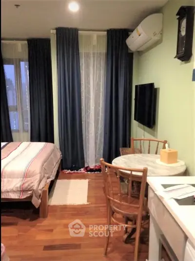 Cozy bedroom with wooden flooring, featuring a small dining area and wall-mounted TV.
