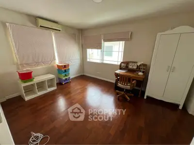 Spacious bedroom with wooden flooring, air conditioning, and ample natural light, perfect for a cozy retreat.