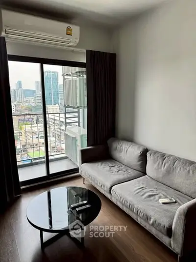 Modern living room with city view, featuring a sleek gray sofa and glass coffee table.