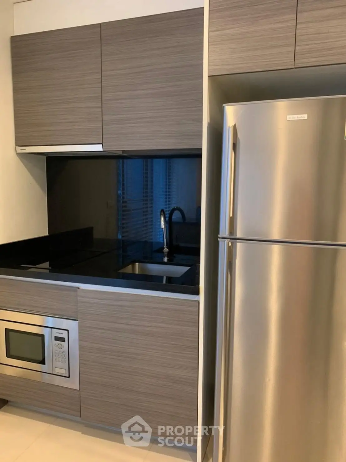Modern kitchen with sleek cabinetry and stainless steel appliances, featuring a built-in microwave and spacious fridge.