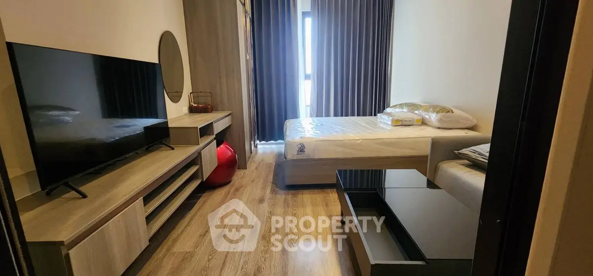 Modern bedroom with stylish decor and large TV, featuring wooden flooring and natural light.