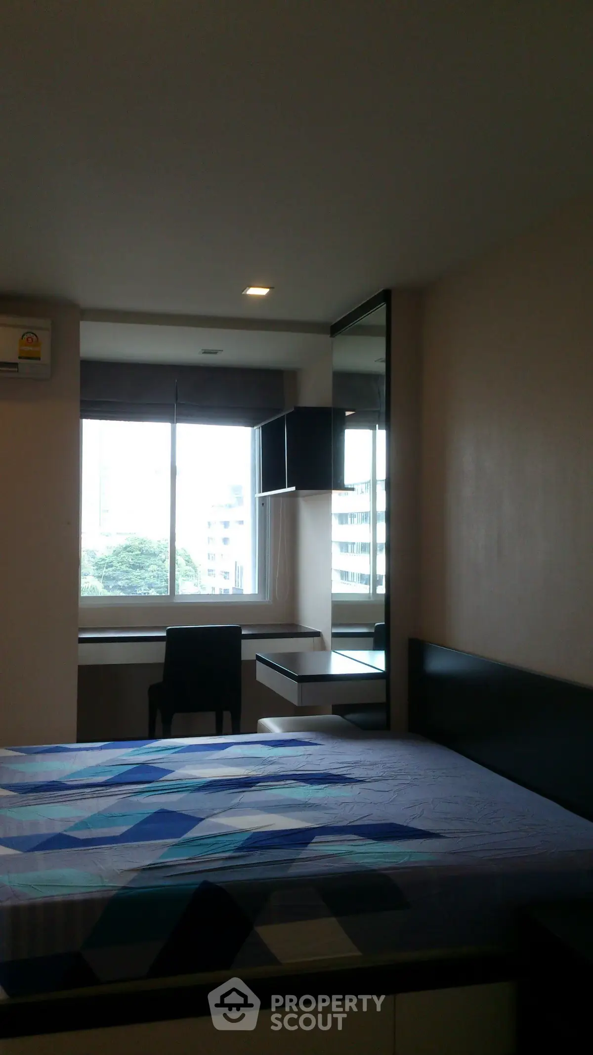 Modern bedroom with large window and city view, featuring a stylish bed and desk area.