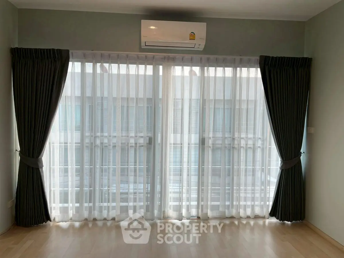 Spacious living room with large windows and elegant curtains, featuring a modern air conditioning unit.