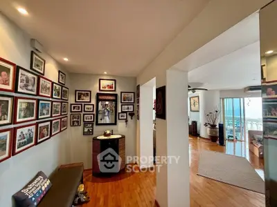 Spacious living area with wooden flooring and photo gallery wall, leading to a bright room with balcony view.