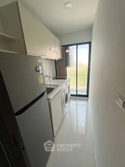 Compact kitchen with modern appliances and sleek design, featuring a washing machine and refrigerator.