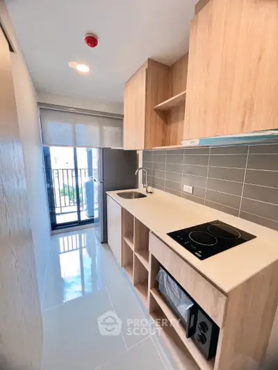 Modern kitchen with sleek design, featuring electric stove and ample storage, overlooking a balcony with natural light.