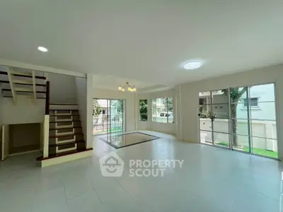 Spacious modern living room with large windows and staircase in a bright home.