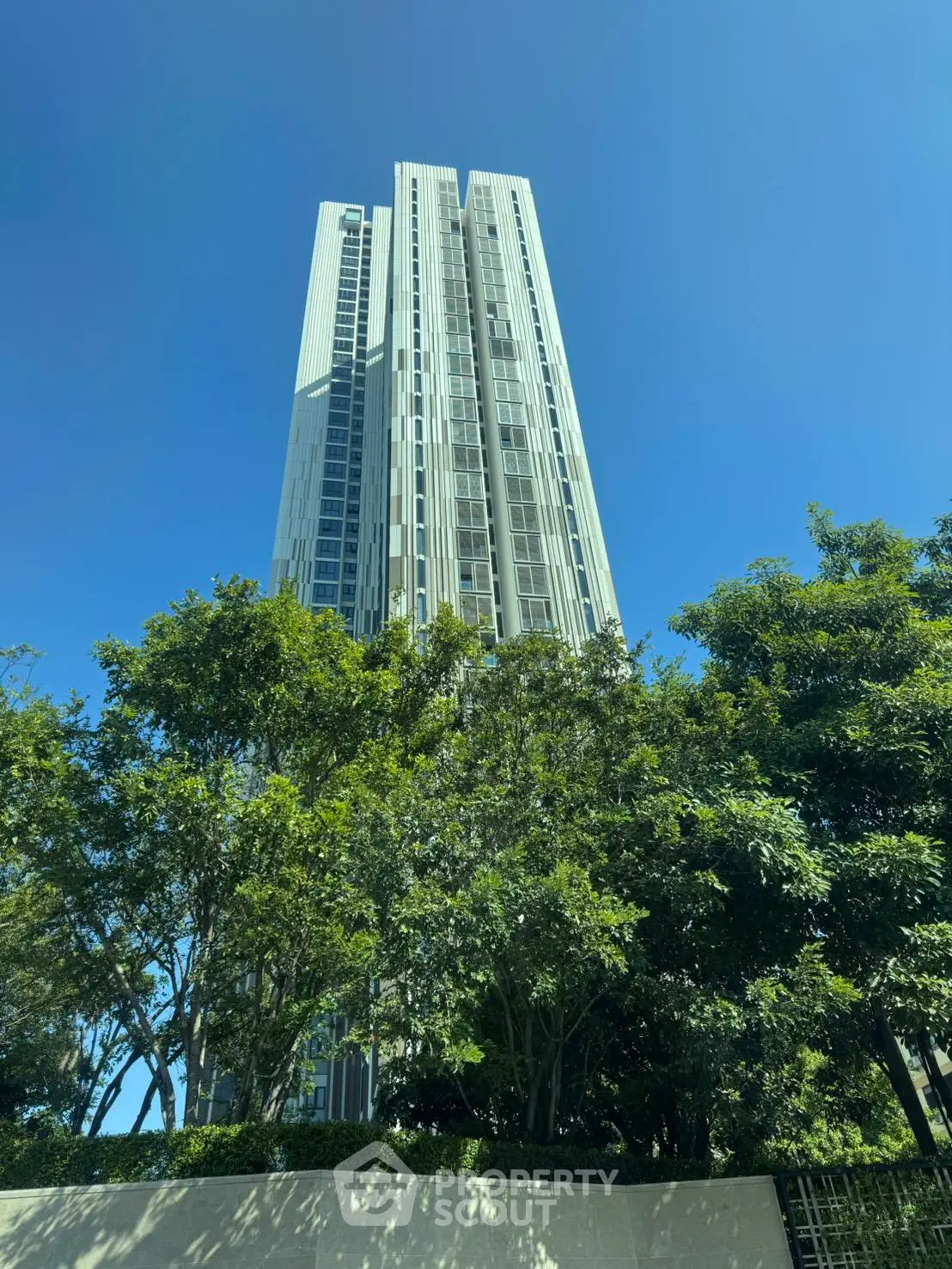 Stunning high-rise building with modern architecture surrounded by lush greenery under a clear blue sky.