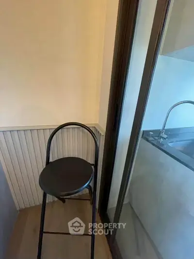 Cozy corner with stool and glass door leading to modern kitchen area.