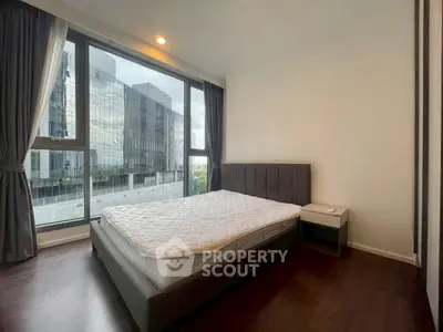 Modern bedroom with large windows and city view, featuring a stylish bed and dark wood flooring.