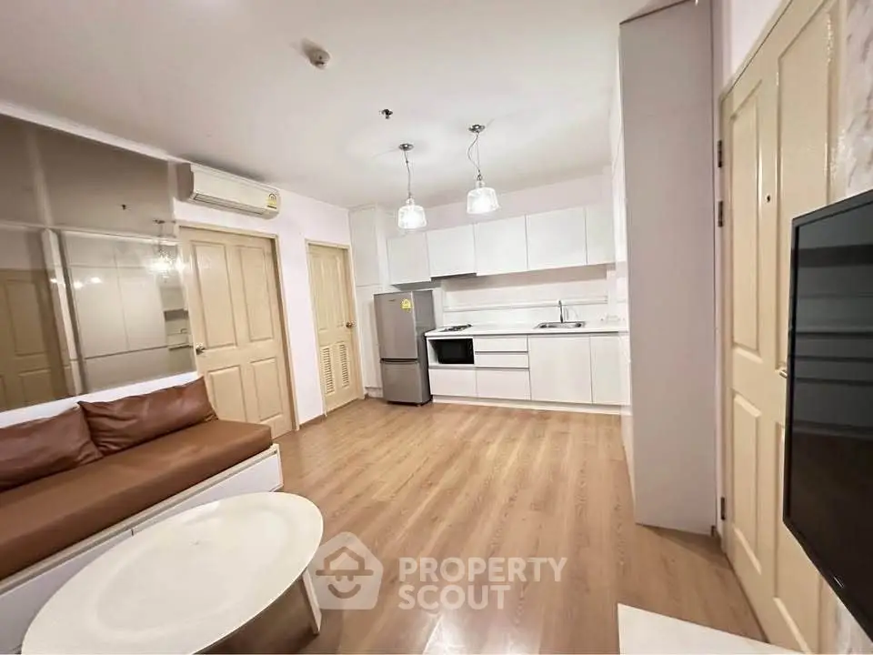 Modern open-layout living room with kitchen, featuring sleek white cabinets and cozy seating area.