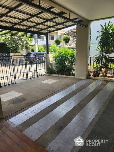 Spacious covered parking area with modern gate and lush greenery