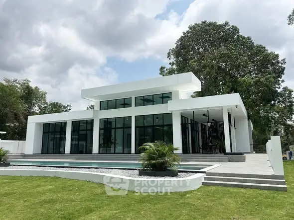 Modern luxury home with sleek architecture and expansive glass windows, surrounded by lush greenery and a pristine lawn.