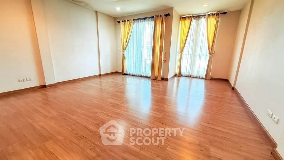 Spacious empty living room with wooden flooring and large windows with curtains.