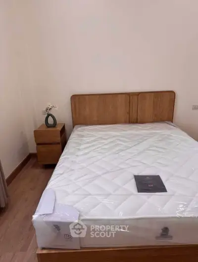 Cozy bedroom with wooden bed frame and nightstand, featuring a new mattress in a minimalist design.
