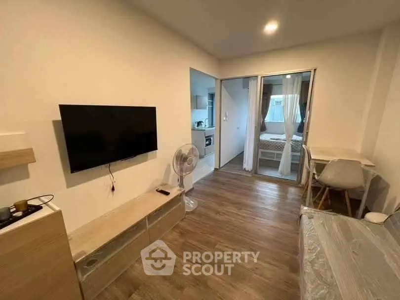 Modern living room with wooden flooring, wall-mounted TV, and open view to bedroom.