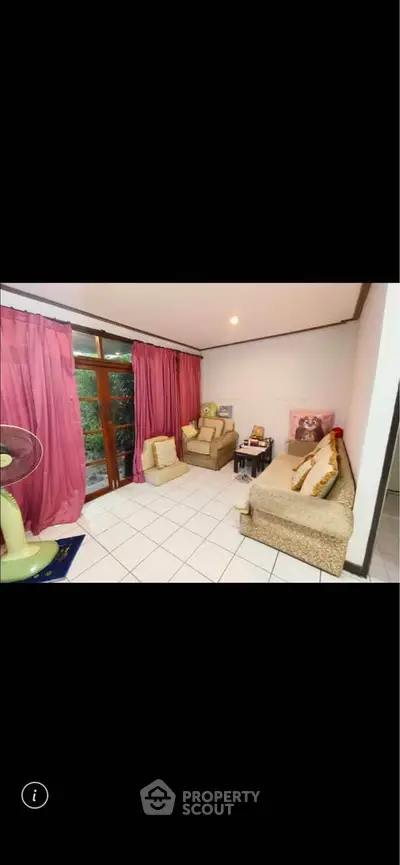 Cozy living room with large windows and pink curtains, featuring comfortable seating and a fan.